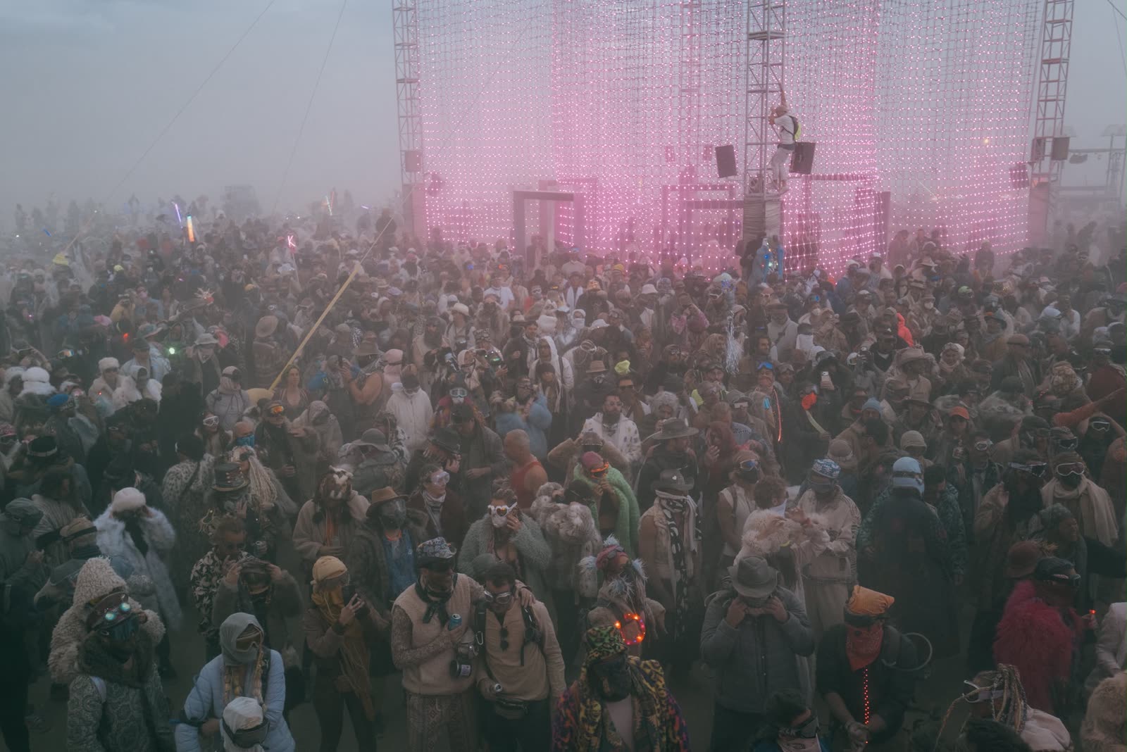 The crowd in front of the cube, lit pink, in the dust